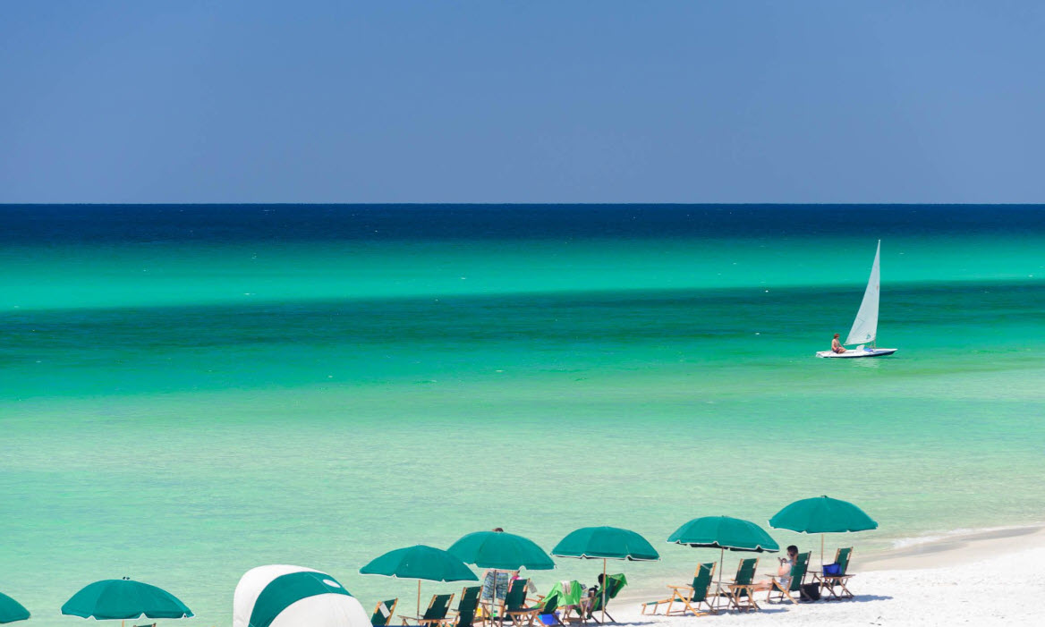 Sailboat beyond a row of green beach umbrellas
