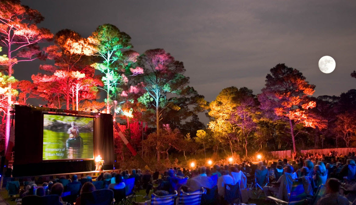 Families watching an outdoor movie beneath a full moon