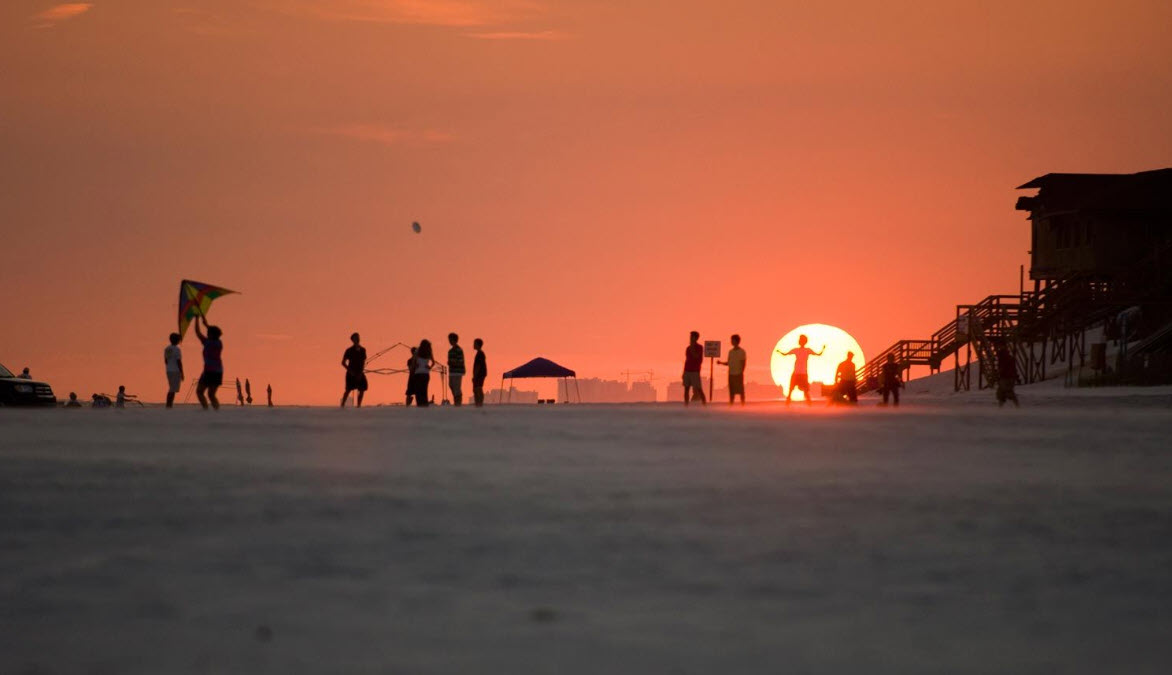 Families silhouetted beside the setting sun on the beach