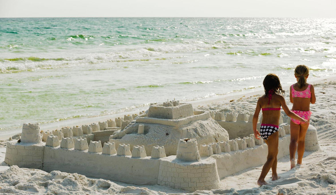 Two children standing beside a large sandcastle