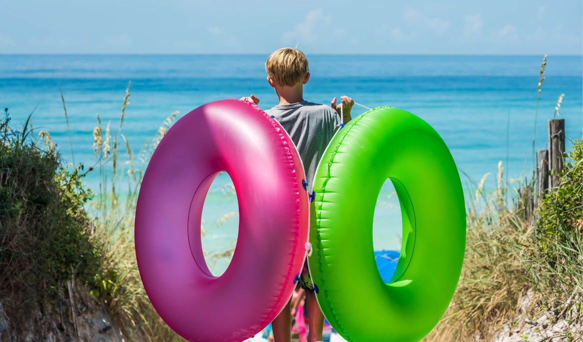 Child carrying bright swim rings toward the Gulf