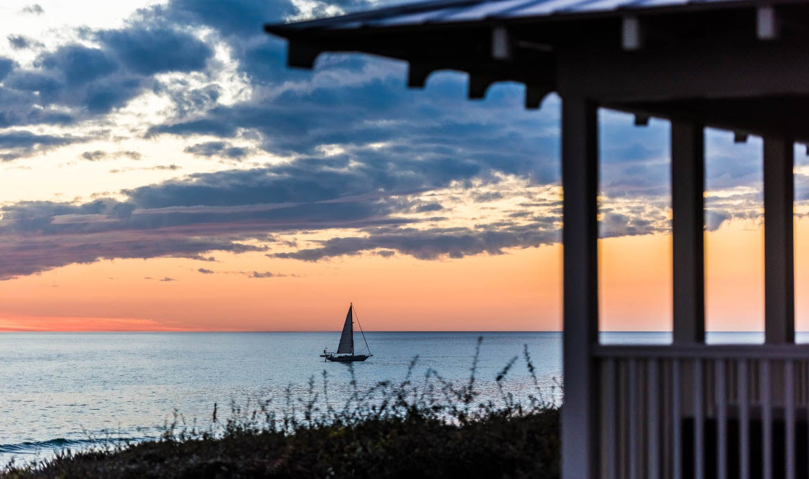 Sailboat at sunset framed by a shaded coastal porch