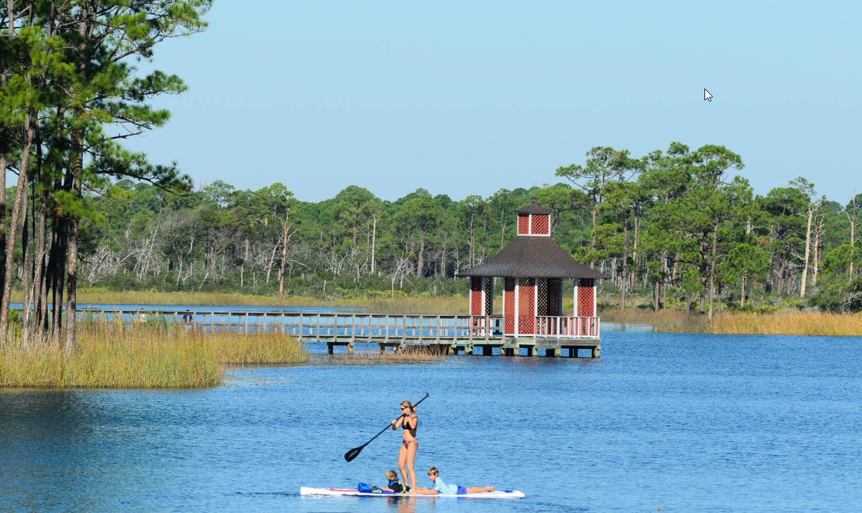 Paddleboarder crossing a coastal lake near a small boathouse
