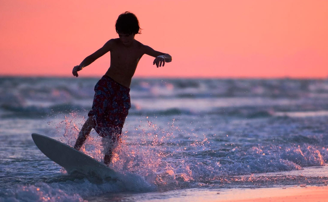 Child skimboarding in the surf at sunset