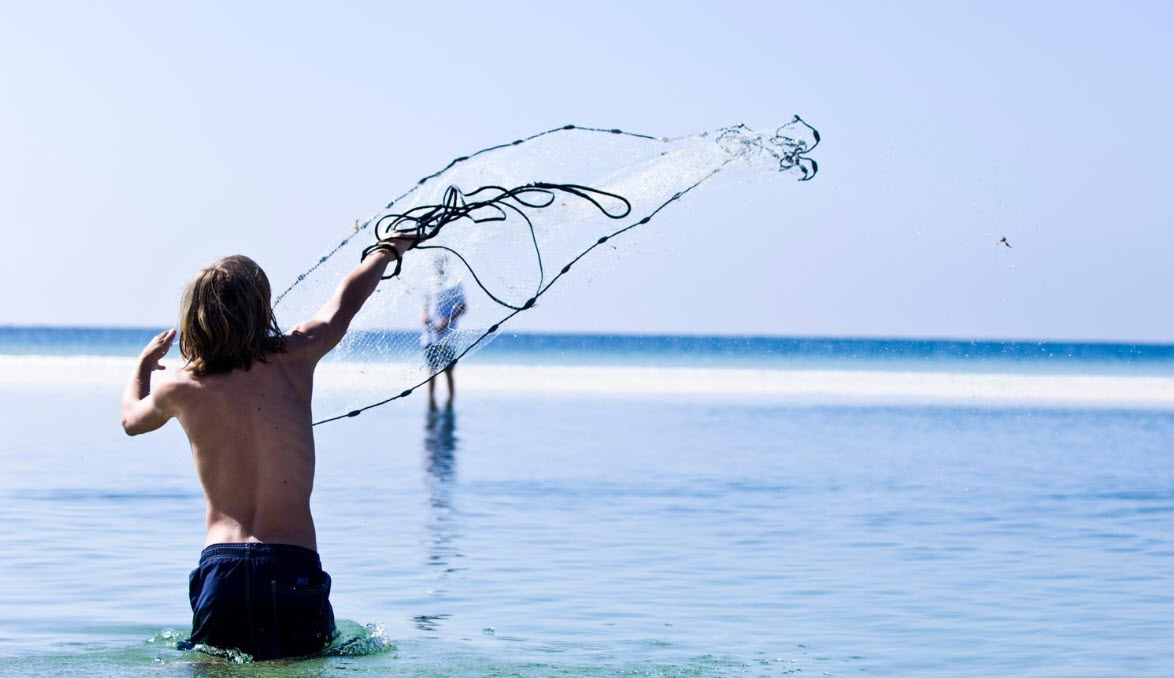 Boy casting a circular fishing net from shore