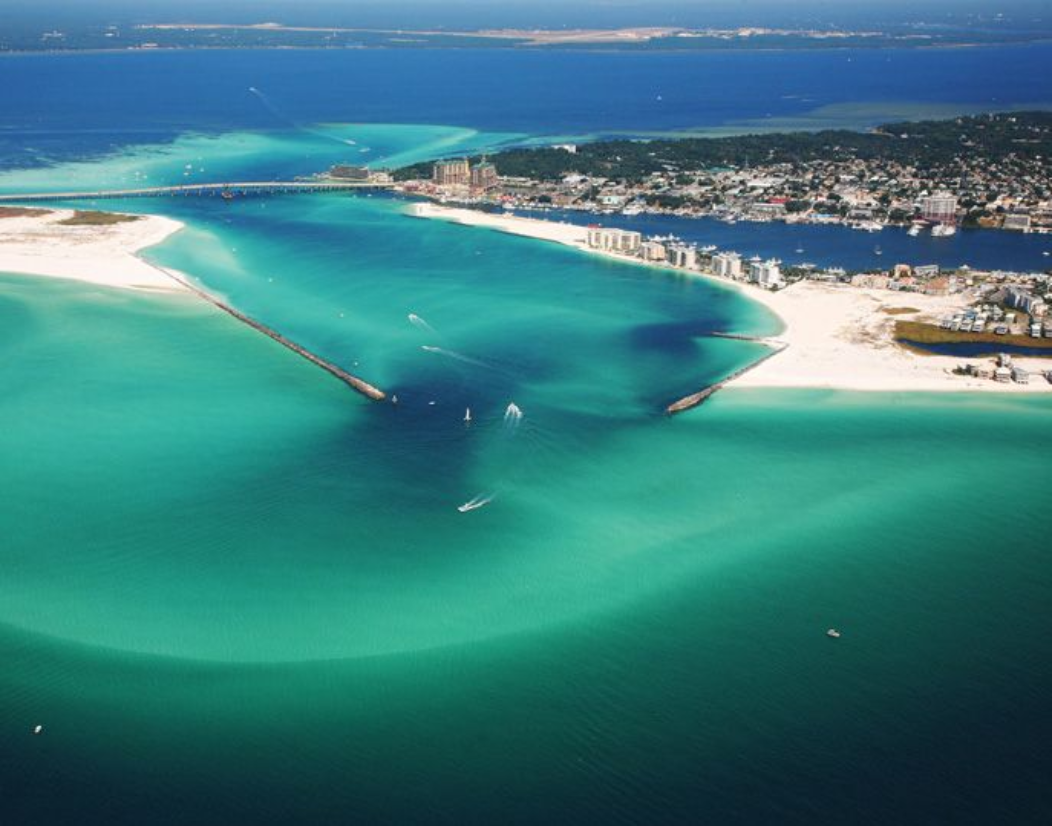 Aerial view of emerald water, white sand, and inlet jetties